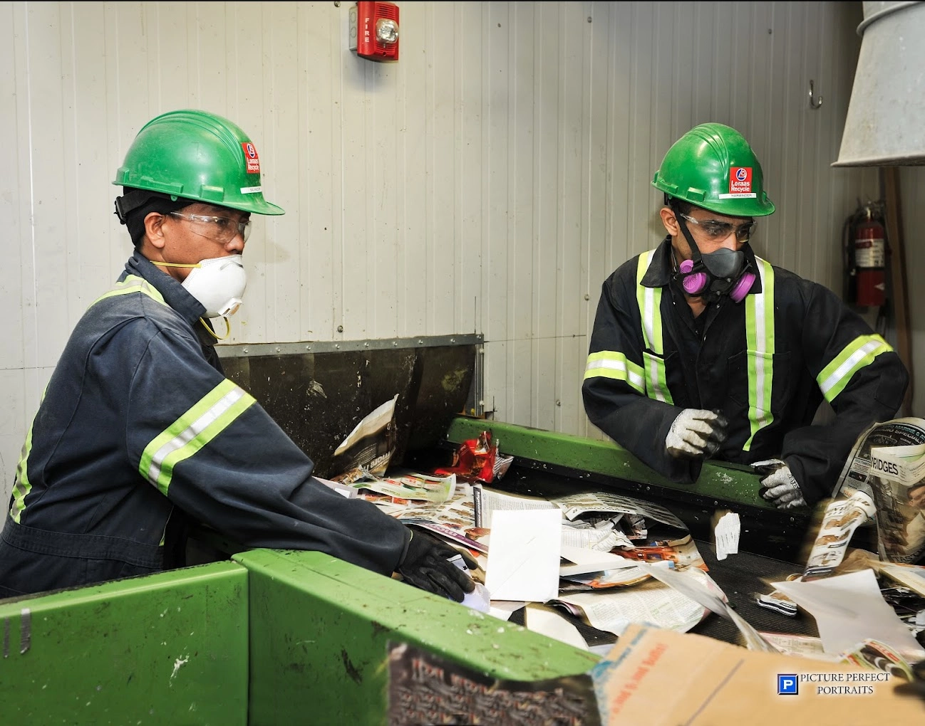 Two workers in hard hats and respirators sorting material on a recycling line