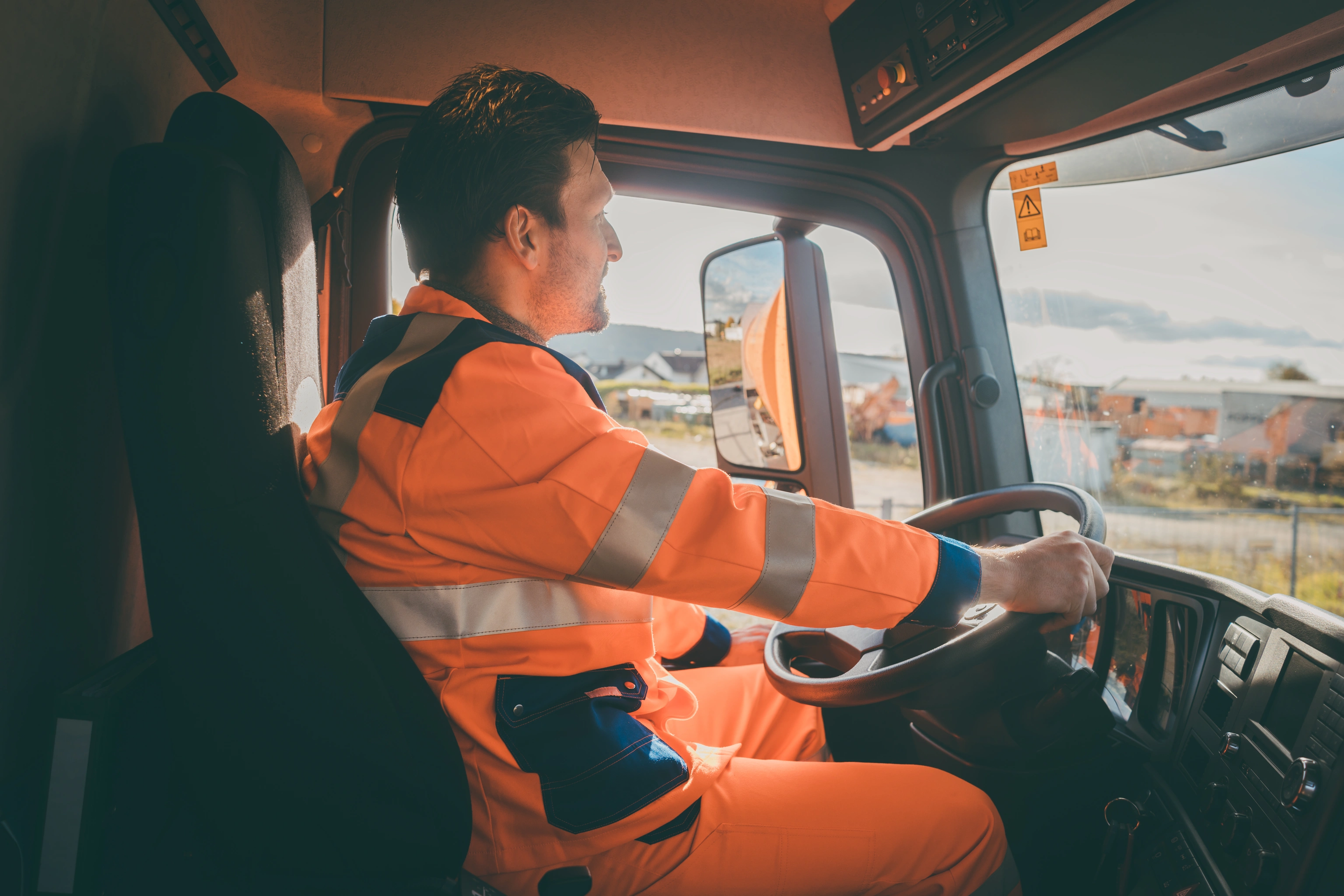 A driver in high-visibility orange coveralls at the wheel of a collection truck