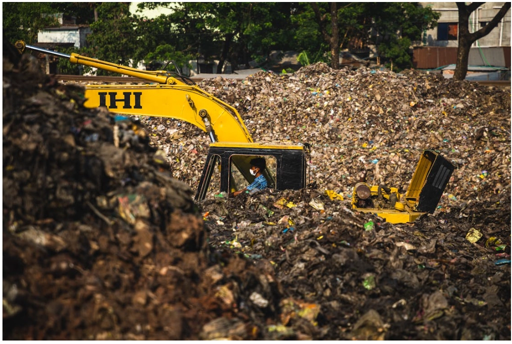 An excavator working in a landfill heaped with mixed waste
