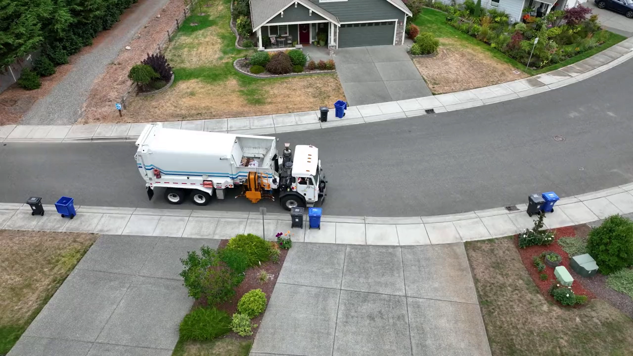 Aerial view of an automated side-loader truck collecting carts on a residential street