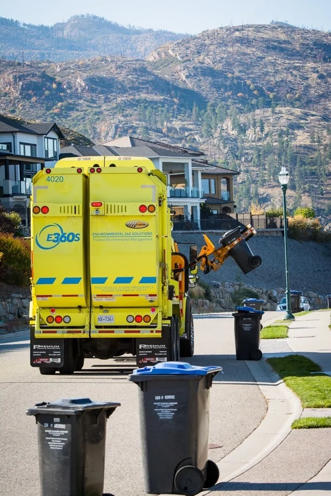 An E360S automated collection truck emptying a residential cart on a hillside street