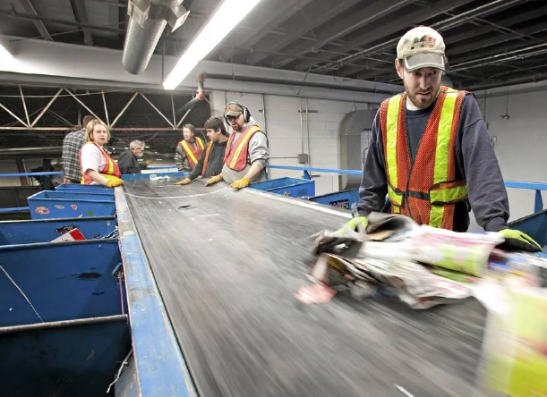 Workers in safety vests sorting recyclables on a conveyor belt at a materials recovery facility