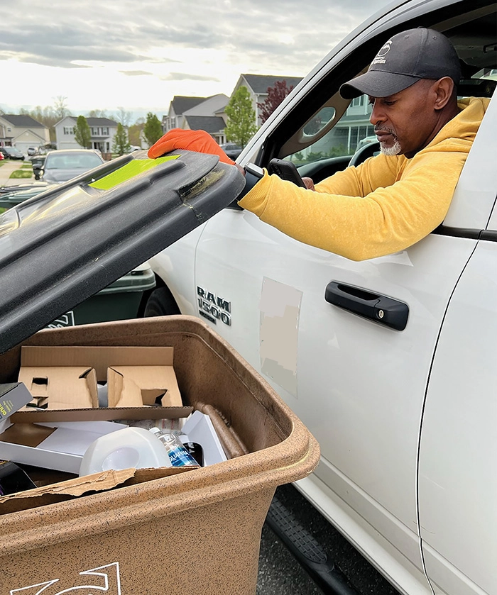 A city worker leaning out of his truck to lift a recycling cart lid and check its contents